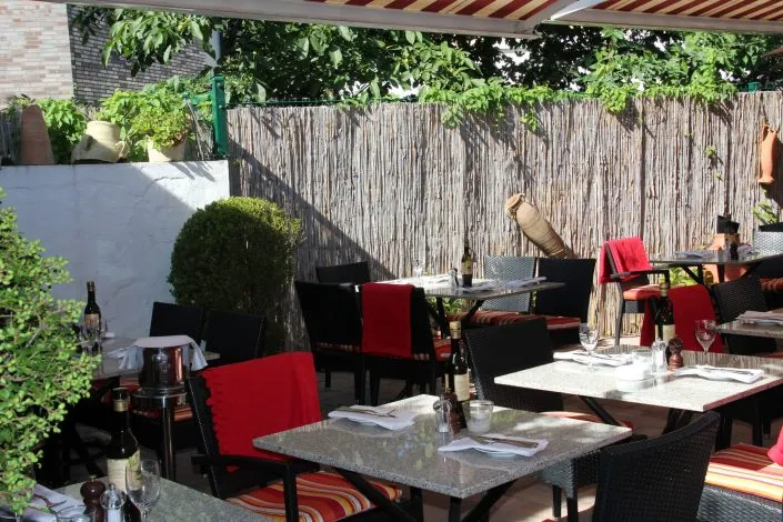 Eingedeckte Tische auf einer schattigen Restaurantterrasse im Freien.