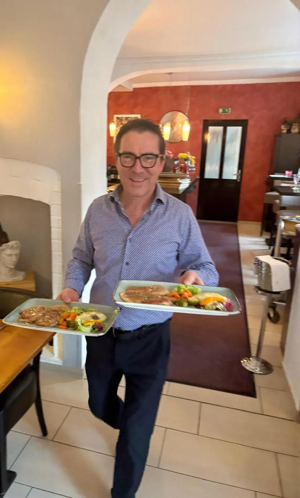 Ein freundlicher Kellner serviert zwei Teller mit frisch zubereiteten Gerichten in einem Restaurant.