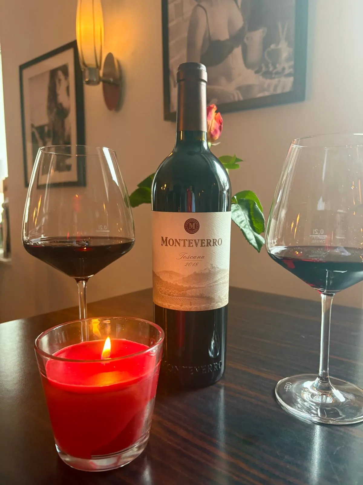 Eine Flasche Monteverro Toscana 2018 Rotwein mit zwei gefüllten Weingläsern und einer brennenden roten Kerze.