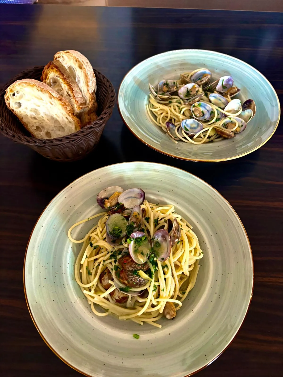 Zwei Teller Spaghetti alle Vongole mit Venusmuscheln und ein Korb frisches Brot in einem Restaurant.