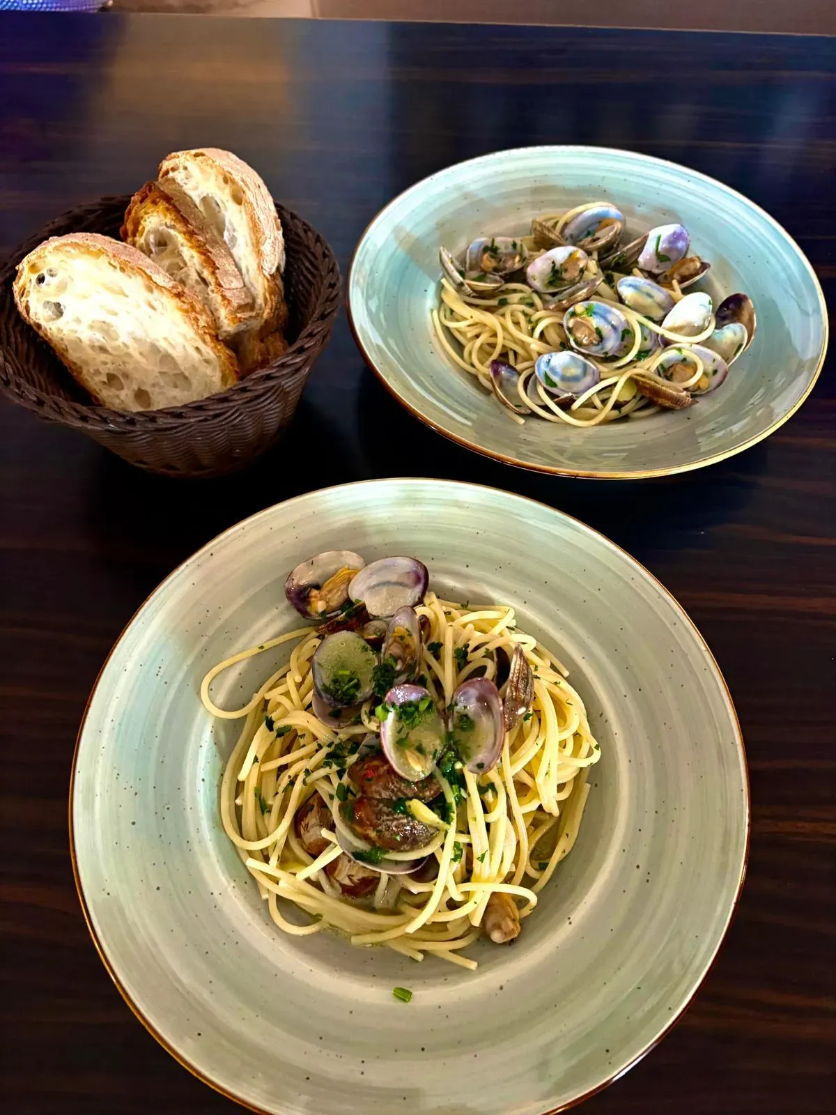 Zwei Teller Spaghetti alle Vongole mit Venusmuscheln und ein Brotkorb.